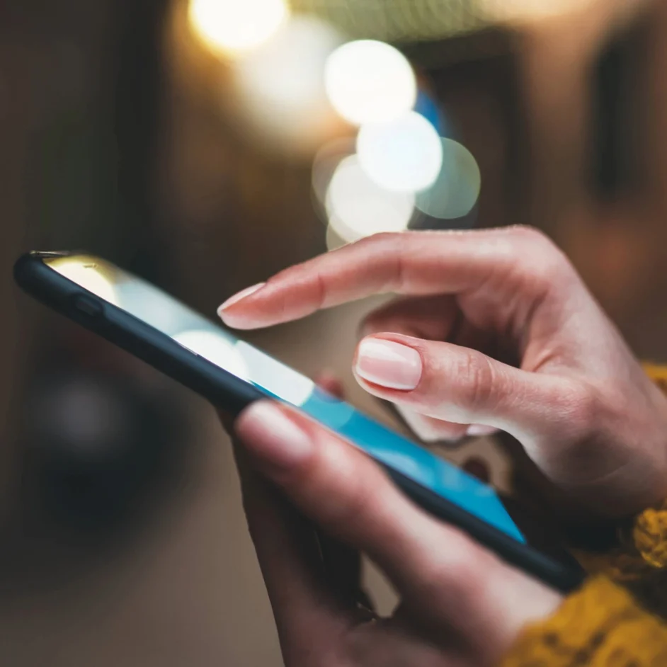 A woman in a yellow jumper checks her phone.