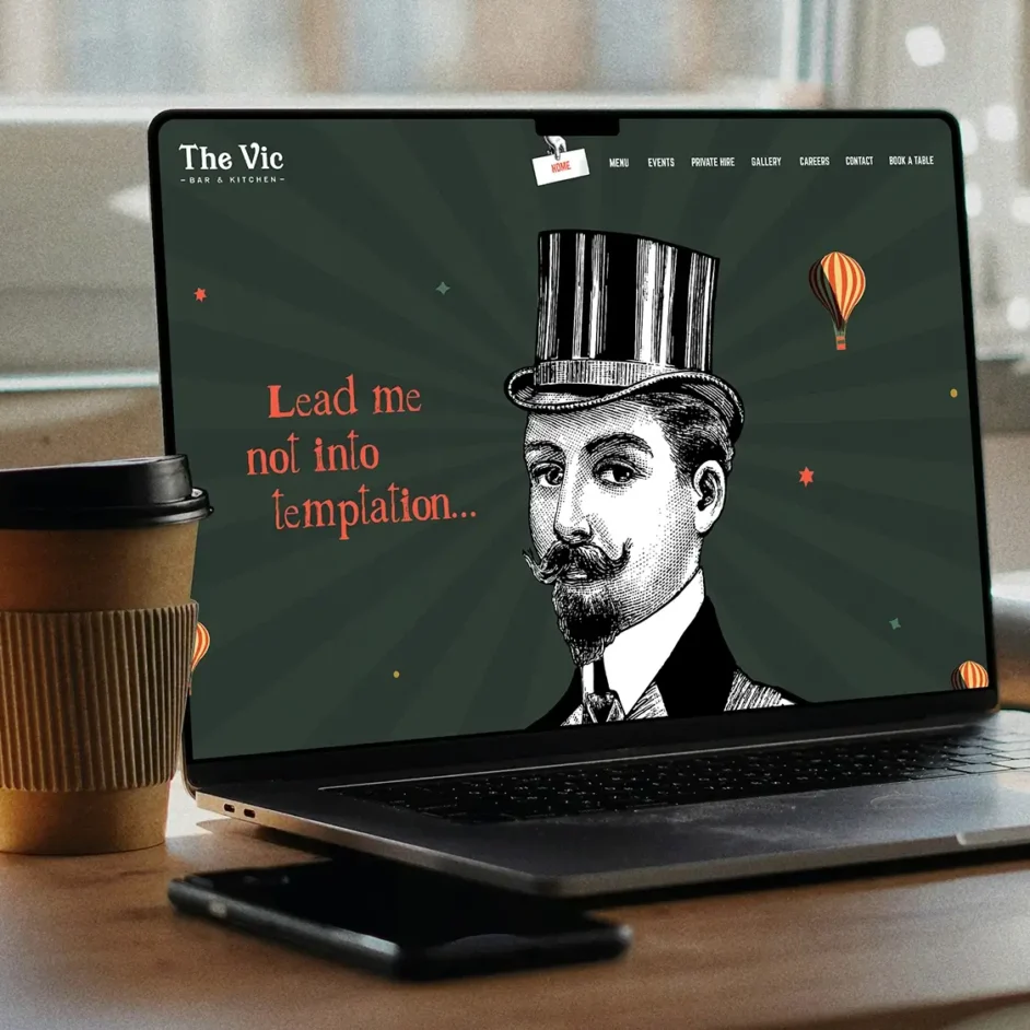 The Victoria Bar & Kitchen's website on a laptop screen with a coffee cup and mobile phone on the table.