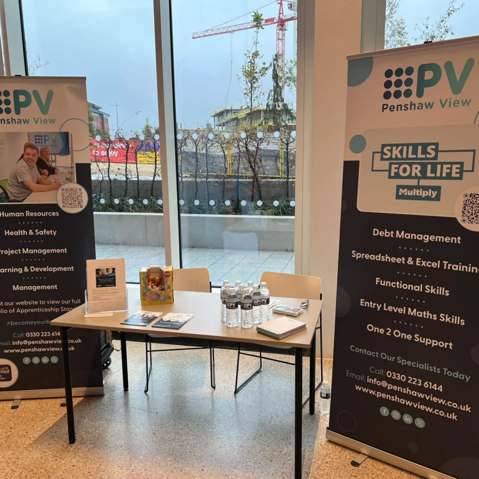 A small table with promotional materials and bottled water at an event between two Penshaw View banners.