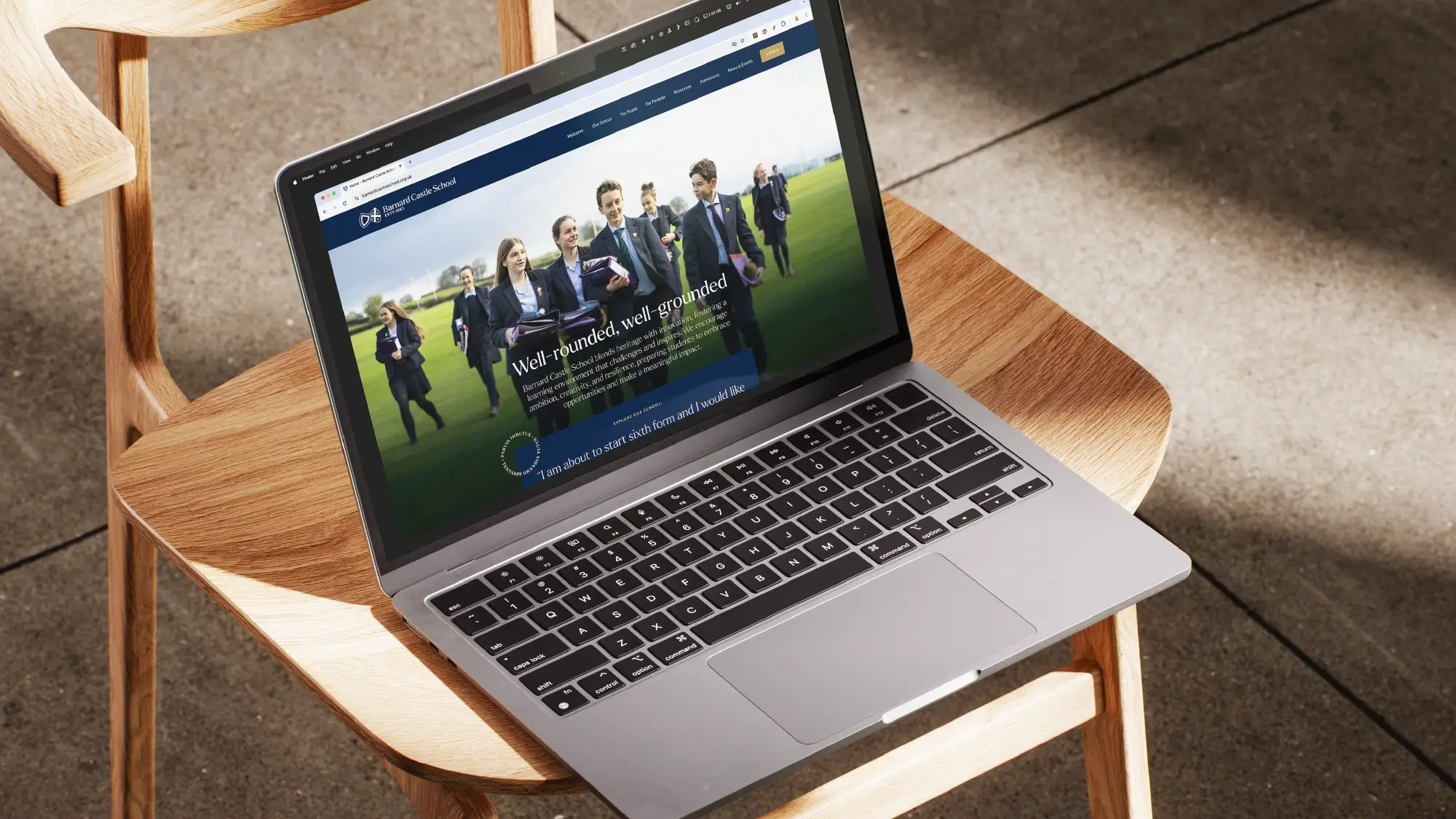 A Macbook on a wooden chair with the Barnard Castle School website open on it.
