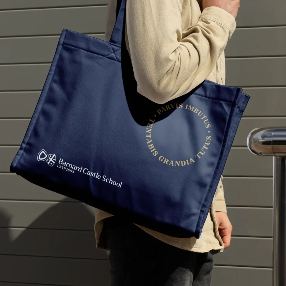 A dark blue tote bag with the Barnard Castle School logo and motto on it.