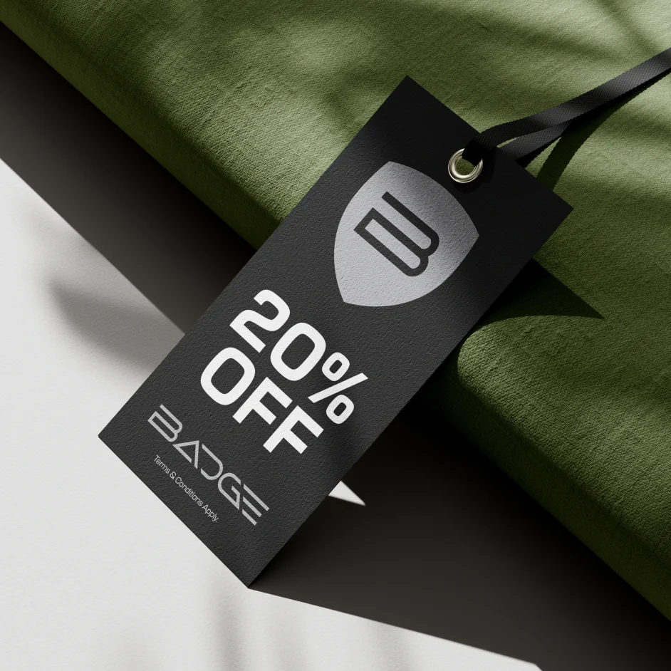 Black branded 20% off label displayed against dappled light and green material in background.