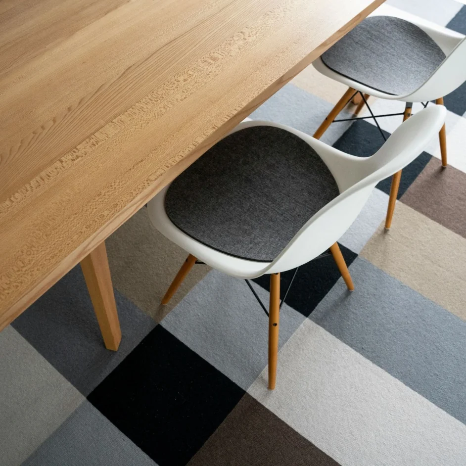 A modern wooden table with scooped white chairs tucked under it, sitting atop a colourful rug.